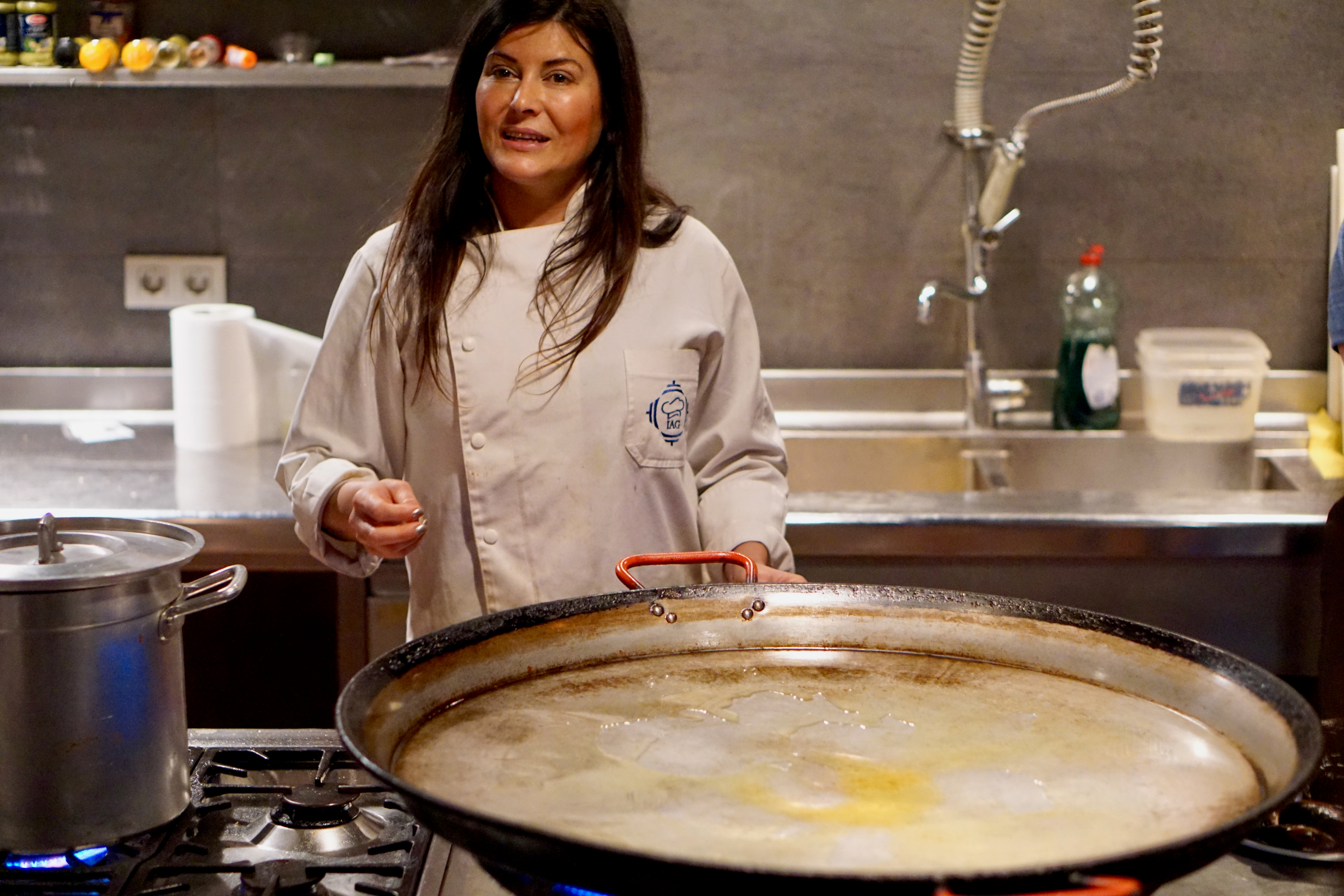 A woman teaching a paella class in Barcelona, Spain in front of a large traditional paella pan